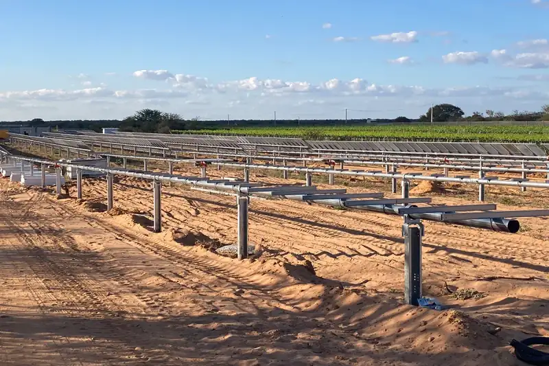 Estruturas de uma usina fotovoltaica de solo ao lado de uma lavoura
