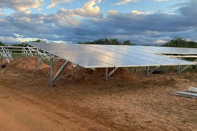 Módulos fotovoltaicos montados em estruturas de solo, com a obra da usina em andamento